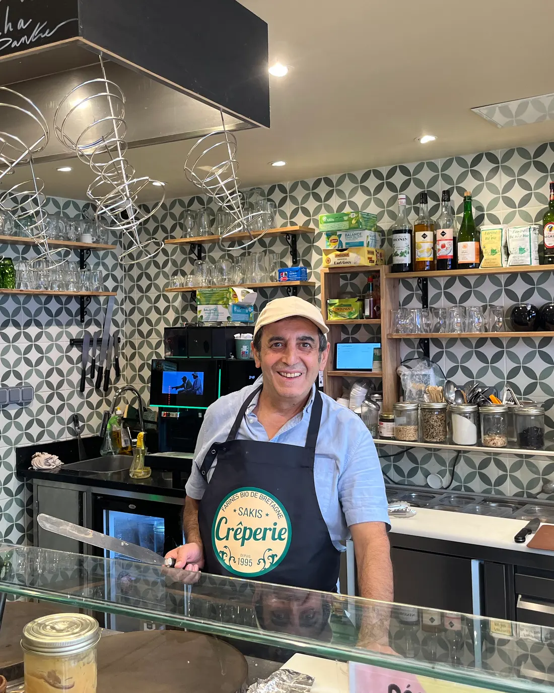 Le crêpier de la Crêperie Sakis derrière son comptoir, tablier « Sakis Crêperie depuis 1995 »